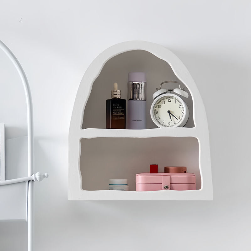 White arched floating shelf with wavy irregular cutouts holding skincare and a clock.