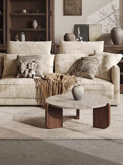 Round organic modern coffee table with three curved wood legs in a neutral living room.