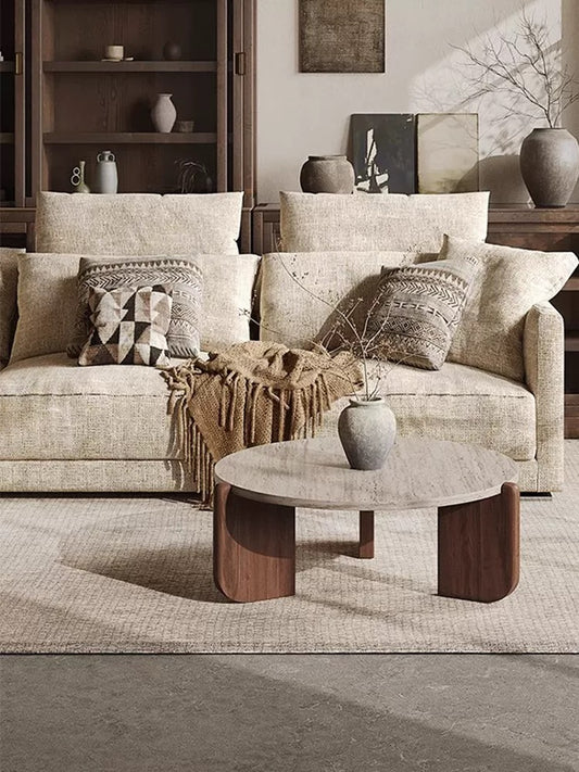Round organic modern coffee table with three curved wood legs in a neutral living room.