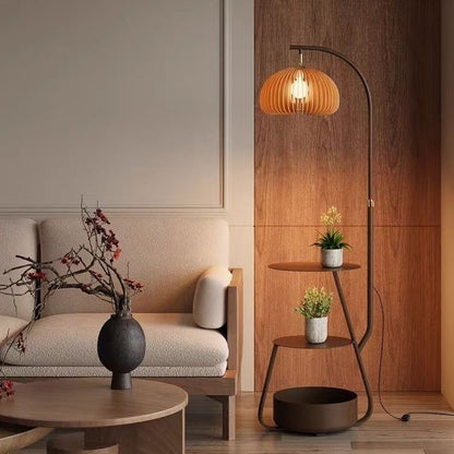 Bronze arc floor lamp with wooden slat shade and 3-tier plant stand shelves next to a sofa.