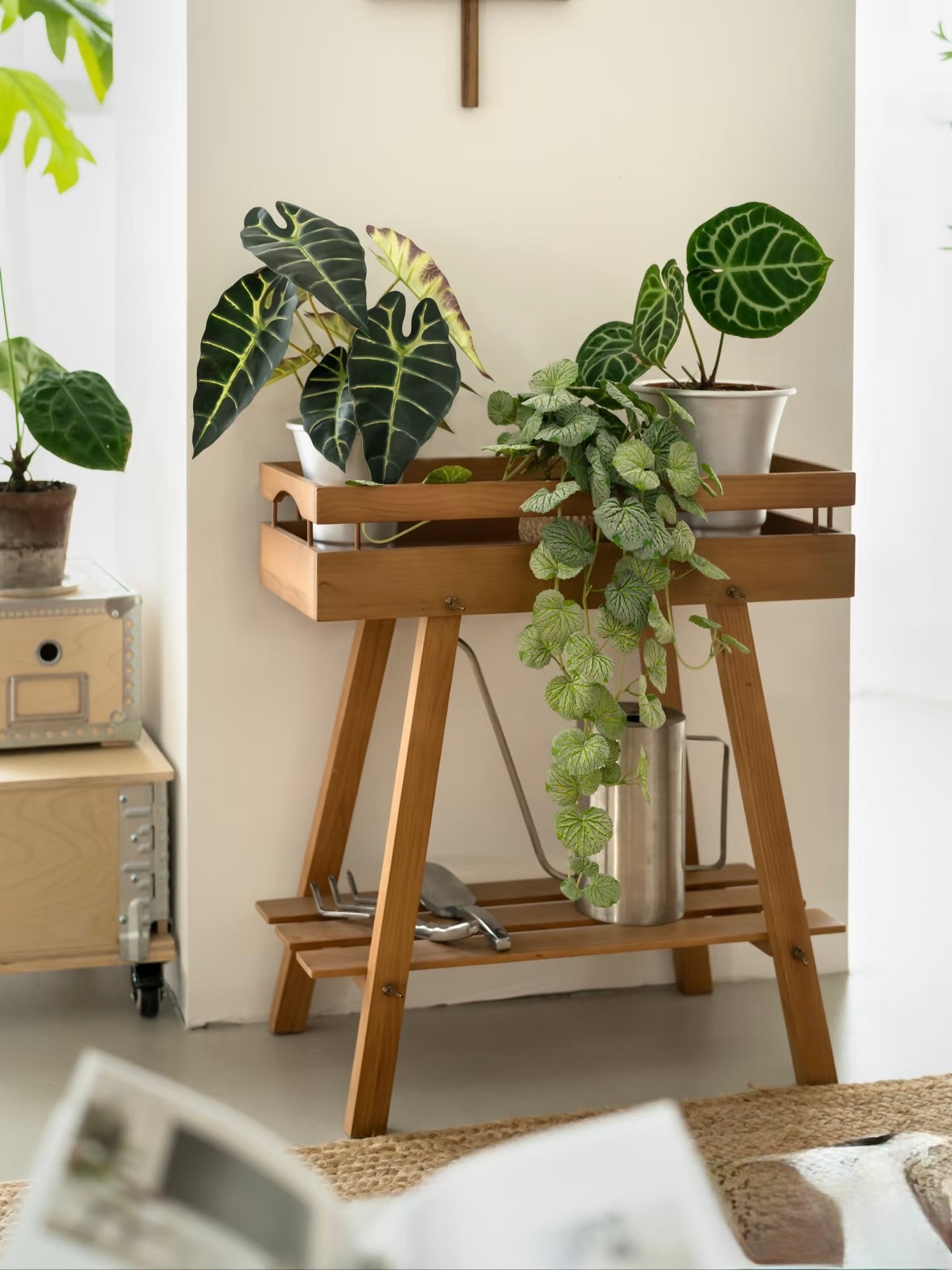 Solid wood plant holder with slatted shelf and tray top in a minimalist white room.